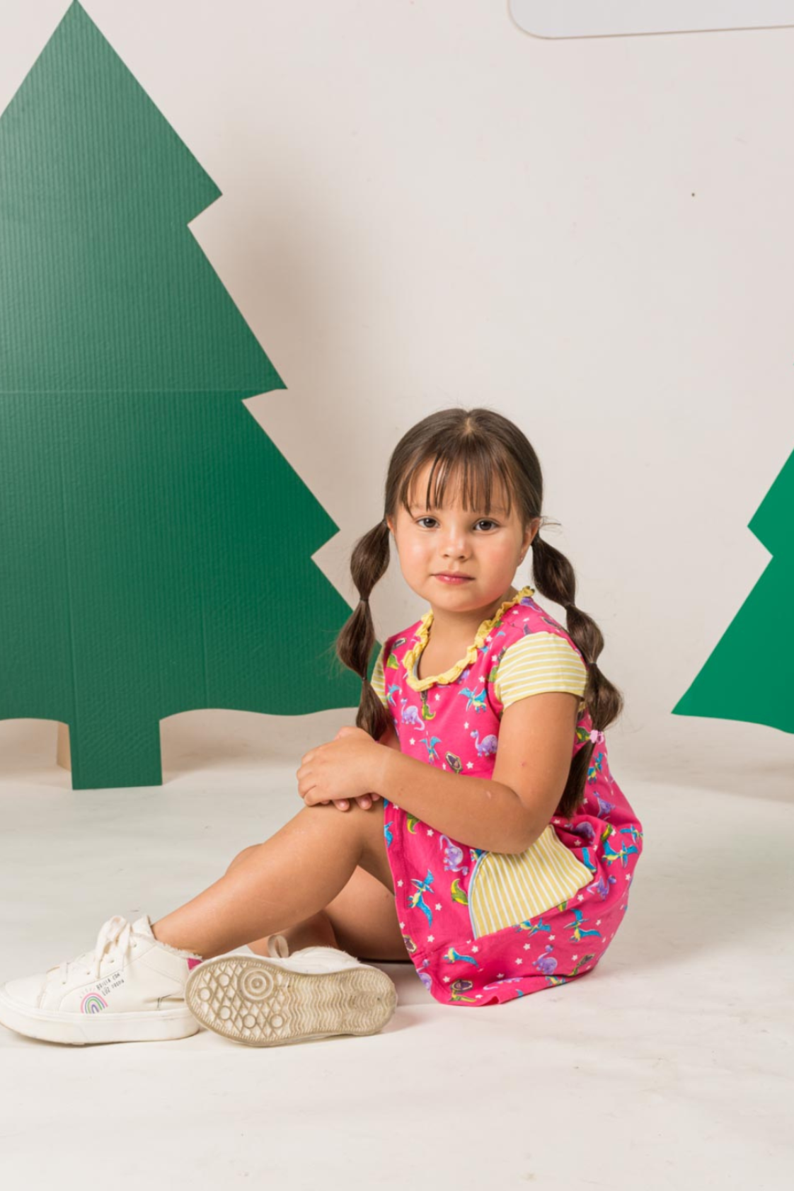 Pastel pink short-sleeve T-style dress featuring a colorful T-Rex and Pterodactyl print, a delicate ruffled collar, and handy striped front pockets.