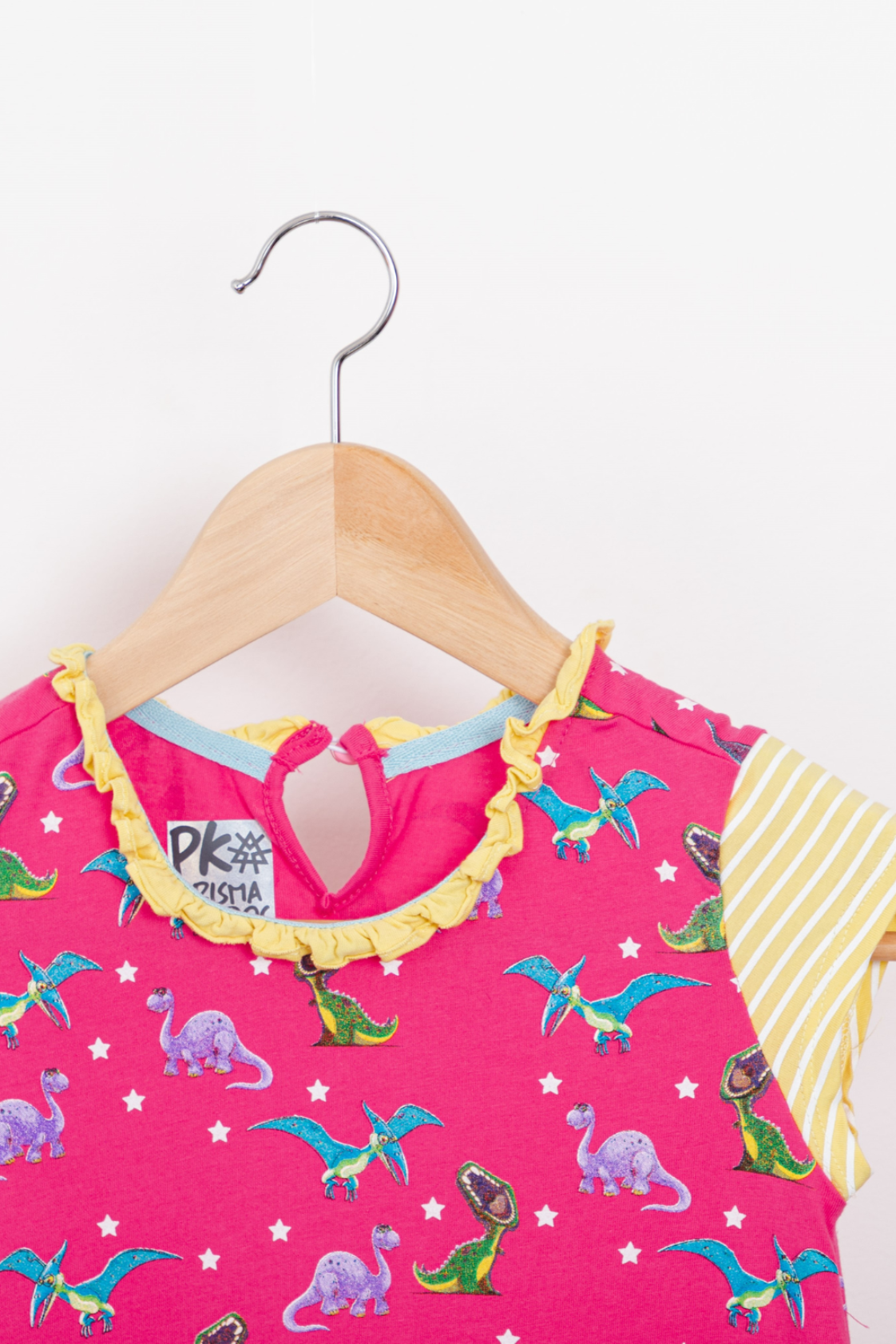 Pastel pink short-sleeve T-style dress featuring a colorful T-Rex and Pterodactyl print, a delicate ruffled collar, and handy striped front pockets.