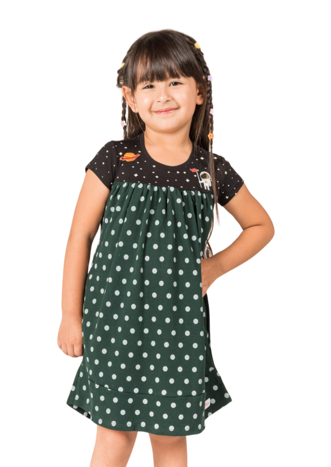 Young girl standing with a playful expression wearing a forest green empire-style dress decorated with astronaut graphics and a constellation-patterned skirt.