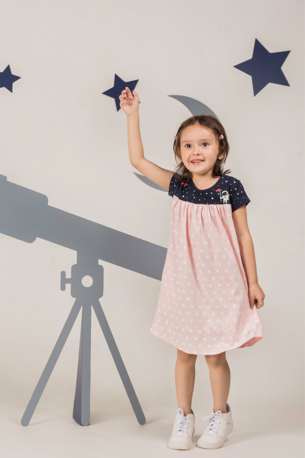 Close up of a soft pink girl's dress with a starry galaxy pattern, detailed Saturn and astronaut prints on the chest, and deep pockets in the skirt.