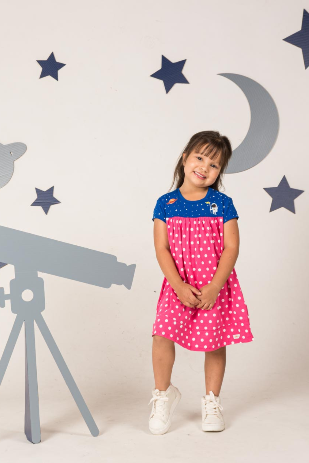 Young girl wearing a vibrant wild berry pink and navy blue empire dress featuring a starry night pattern with detailed astronaut and Saturn prints.