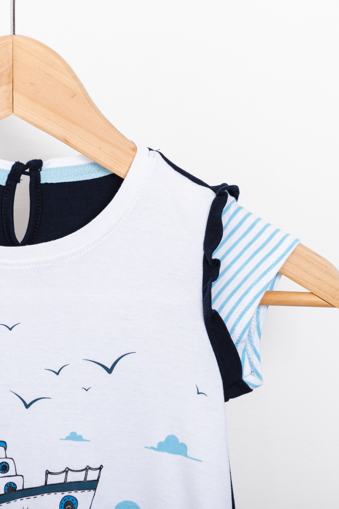 White front, ocean-blue back girl dress with an illustrated sailboat print, featuring textured ruffle sleeves and side pockets.