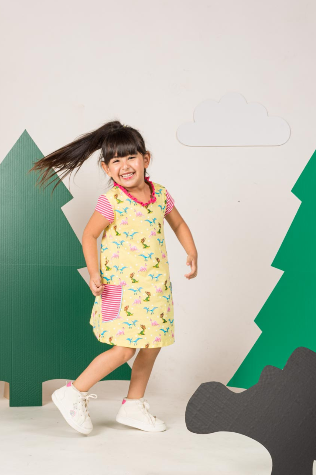 Bright yellow short-sleeve dress for girls featuring a vibrant colorful dinosaur print, a fine ruffled neckline, and horizontal striped front pockets.