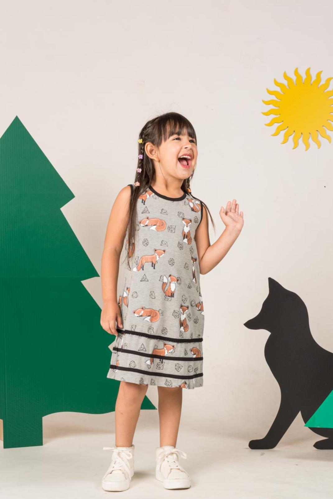 Front view of a grey sleeveless girl's dress featuring an orange fox and gemstone print pattern, styled with a keyhole back neck button amd apliques