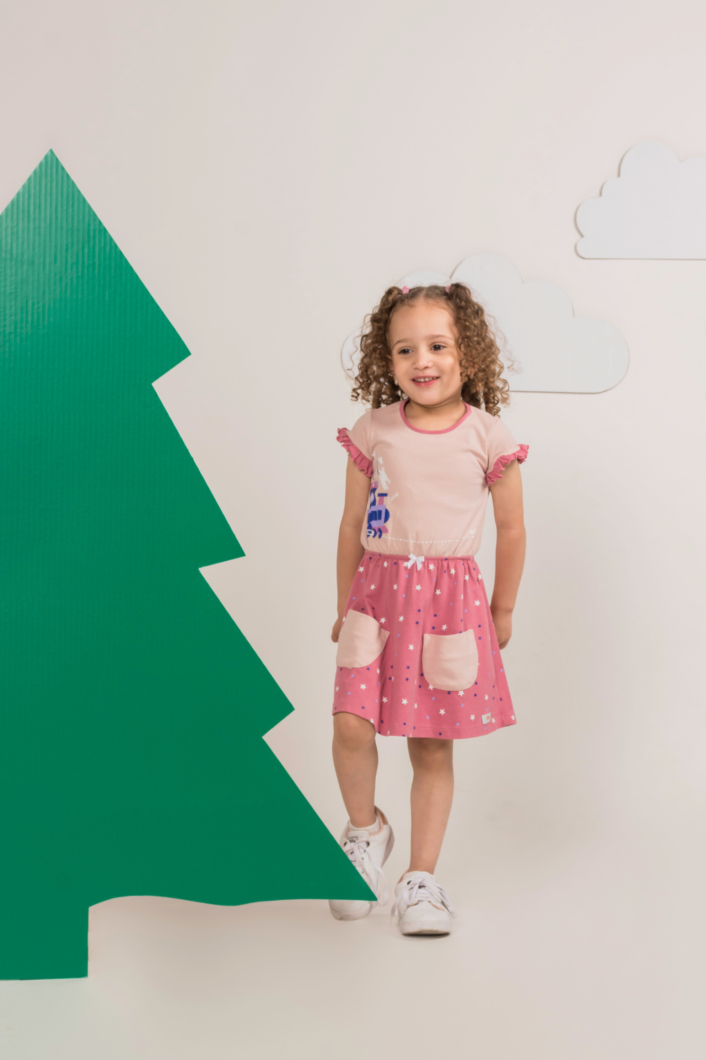 Little girl in a pink short-sleeve dress featuring a geometric train appliqué on the bodice, a star-print skirt, lace waist trim, and side pockets.