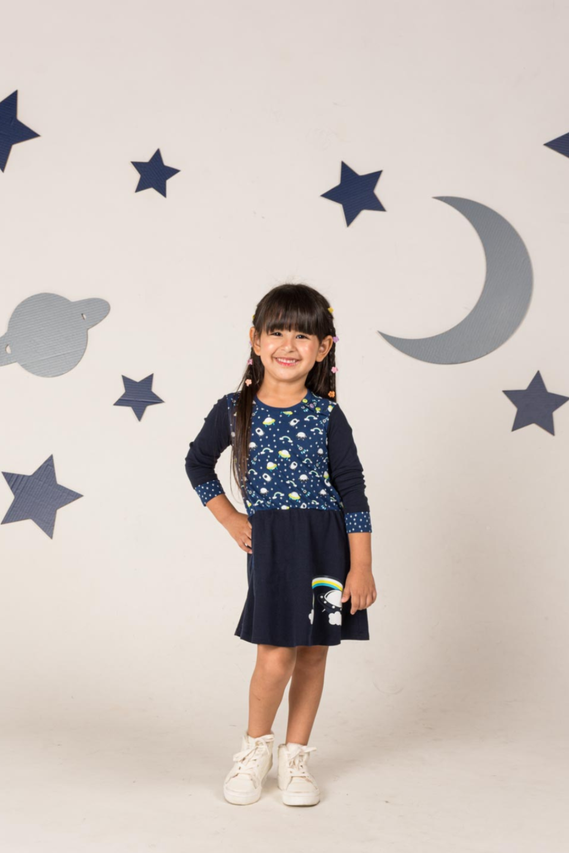 Deep blue girl's dress with 3/4 length sleeves featuring a whimsical design of vibrant rainbows, flying saucers, and rockets with side pockets.