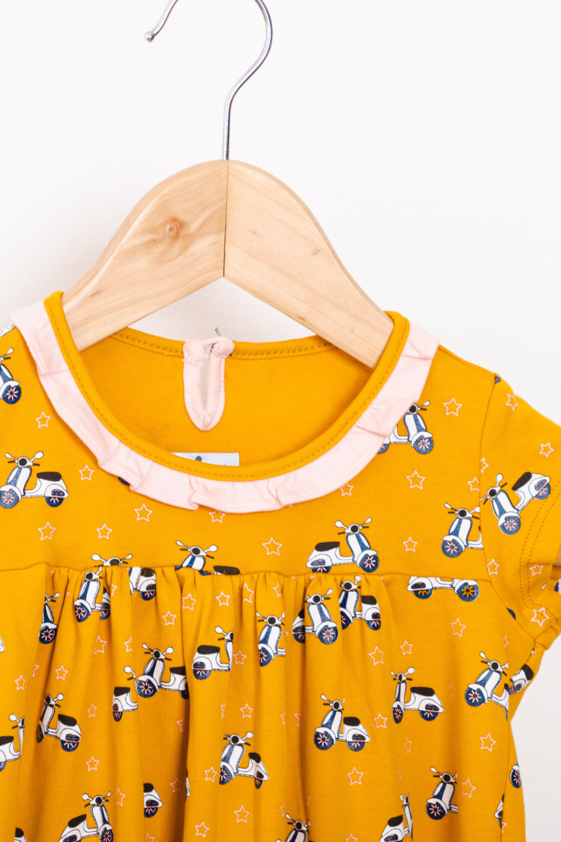 Cheerful yellow empire-silhouette dress for kids featuring a retro scooter print pattern, short sleeves, a ruffled collar, and star-lined pockets.