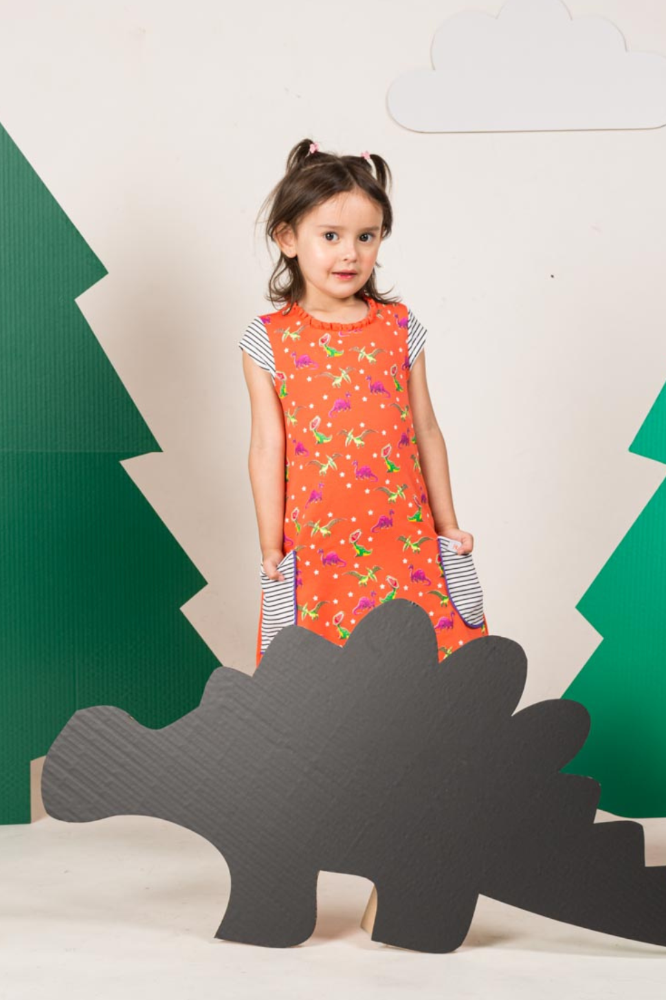 Little girl wearing a coral-colored children's dress with a playful dinosaur print